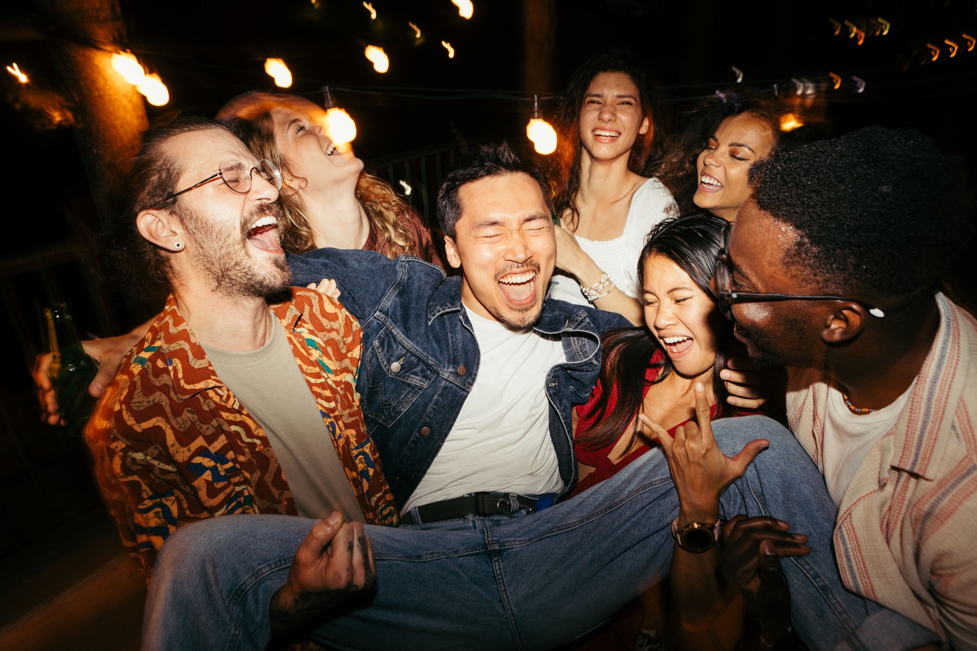 Friends lift their male friend at the night open-air rooftop party.